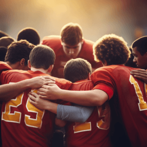 A group of young football players in red jerseys huddle together, with one player's arm around another's shoulders, conveying a sense of teamwork and camaraderie.